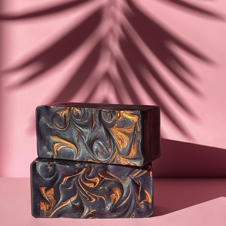 stalk of black soap bars with golden swirls on a peach color background and tropical leaf shadow